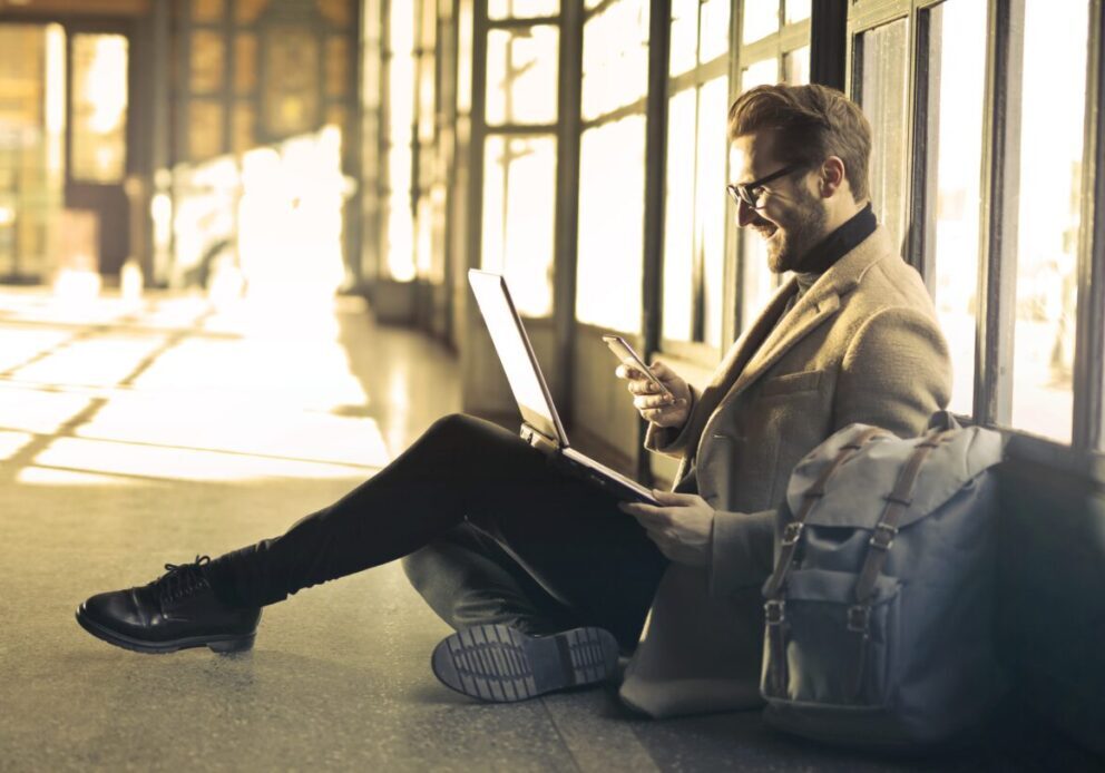 Man sitting with laptop and phone, smiling.
