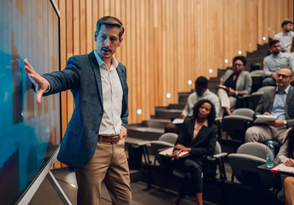 Man giving a presentation to an audience in a wood-paneled room.