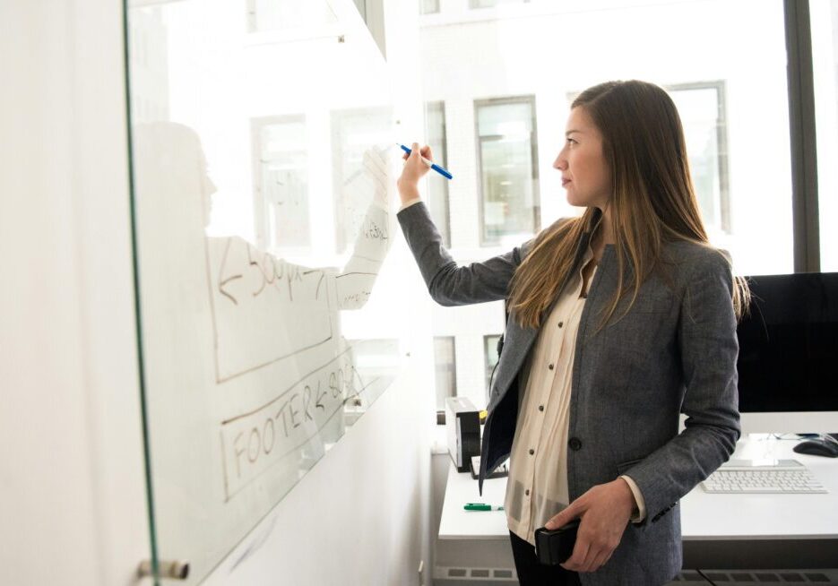 Woman writing on a whiteboard in office.
