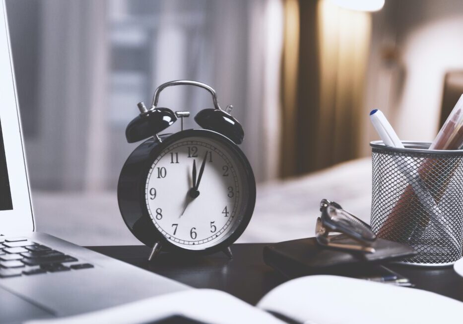 Clock and laptop on a desk.