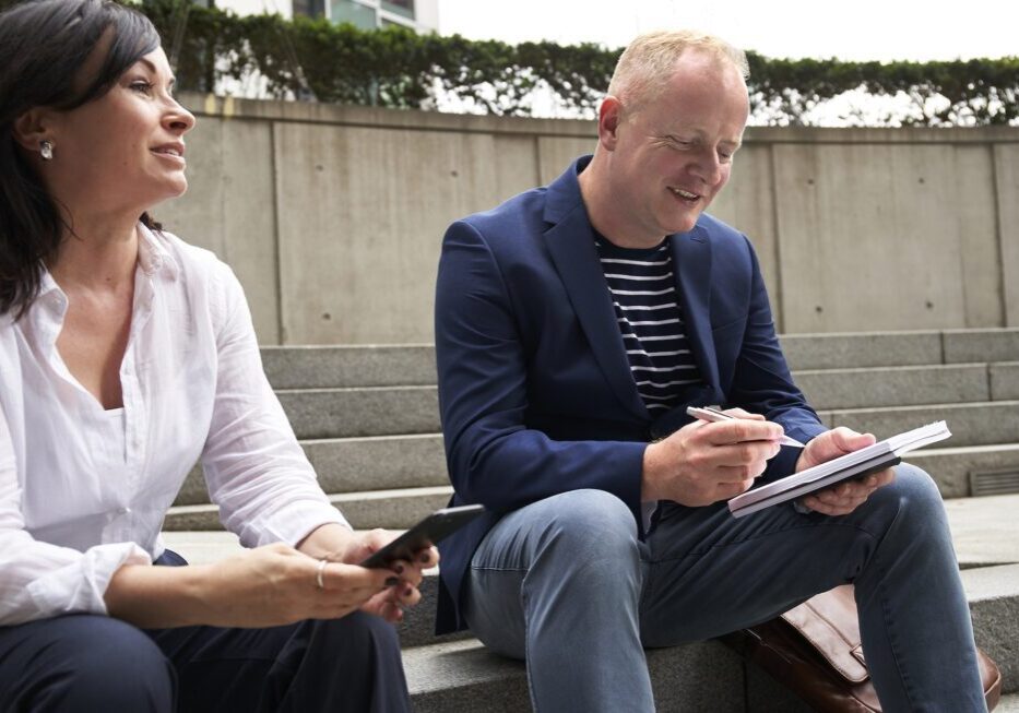 Two people sitting outdoors, writing notes.