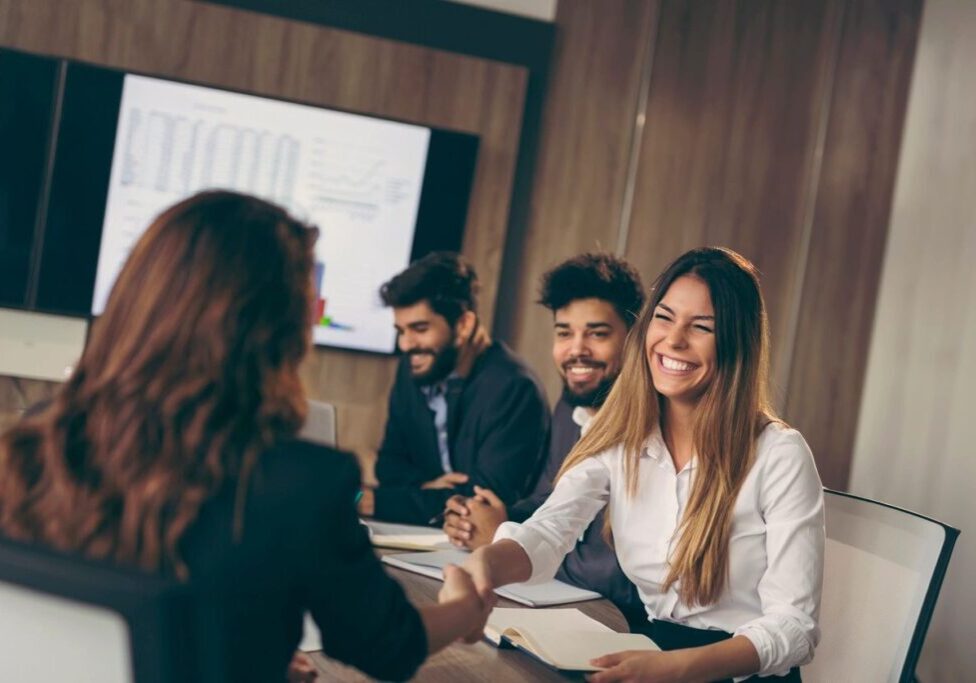 Smiling colleagues shaking hands in meeting room.